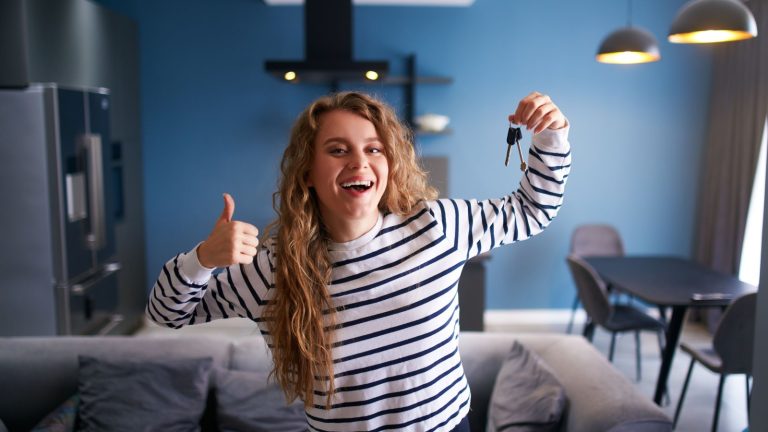 Szczęśliwa kobieta pokazująca klucze do nowego domu lub mieszkania w nowoczesnym wnętrzu. Kobieta najemca z nowymi kluczami do domu przenosi się do najmu. Pani kupiła nieruchomość, przeprowadza się. Koncepcja własności.