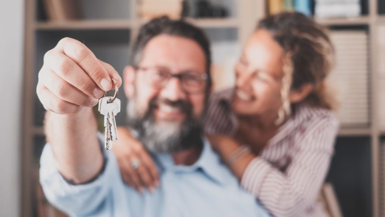 Nacisk na klucze, trzymane przez podekscytowanych młodych małżonków właścicieli domów. Szczęśliwa para małżeńska świętująca przeprowadzkę do nowego domu, demonstrująca klucze, stojąca w mieszkaniu, koncepcja kredytu hipotecznego na nieruchomości.